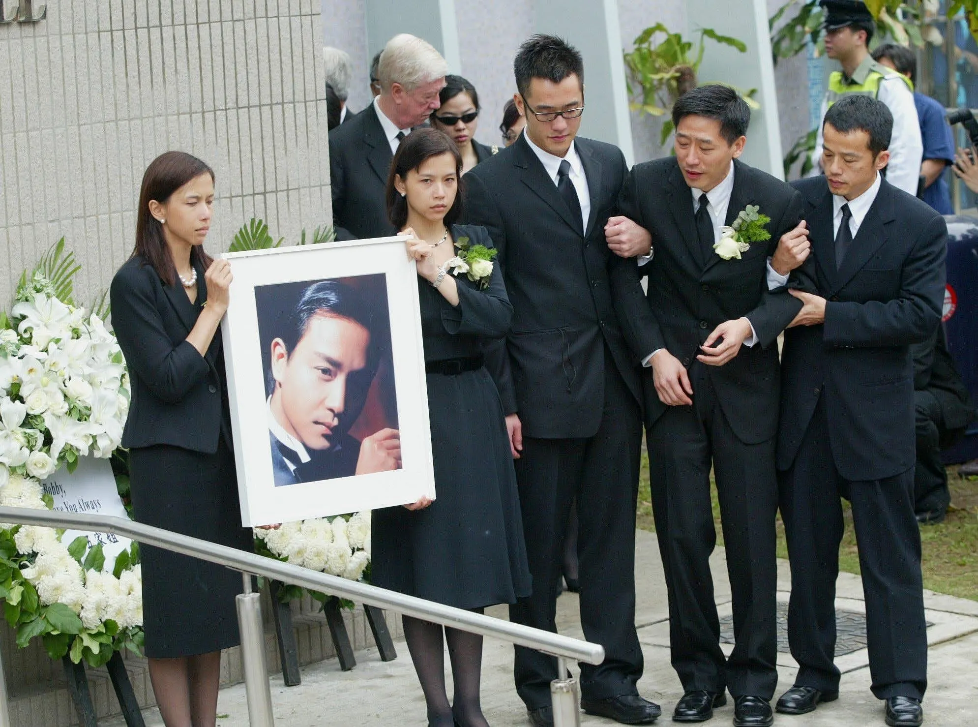 張國榮在演藝行業有重大成就，是不少人的偶像，可是在2003年，他在香港文華東方酒店墜下身亡，消息震撼圈內外。他的葬禮於香港殯儀館舉行，由唐鶴德以至親的身分與親友打點身後事。大批歌迷聚集於殯儀館外，到場的明星眾多，如他生前的好友梅艷芳，也悲痛至泣不成聲，多家電視台均現場直播報導葬禮實況。（視覺中國）
